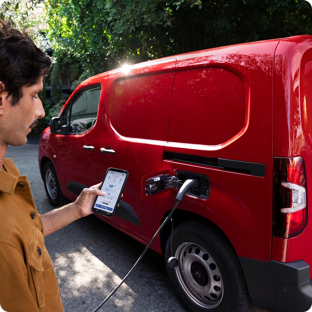Zijaanzicht in driekwart perspectief van een Citroën ë‑Berlingo Van die wordt opgeladen bij een openbaar laadpunt, met focus op praktisch elektrisch gebruik, connectiviteit en dagelijks gemak.