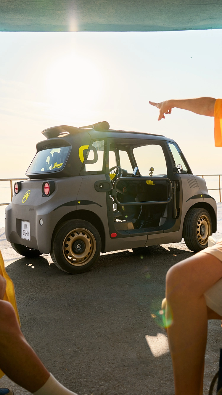 Zijaanzicht van de Citroën Ami aan het strand met compact elektrisch design voor zomerse mobiliteit.