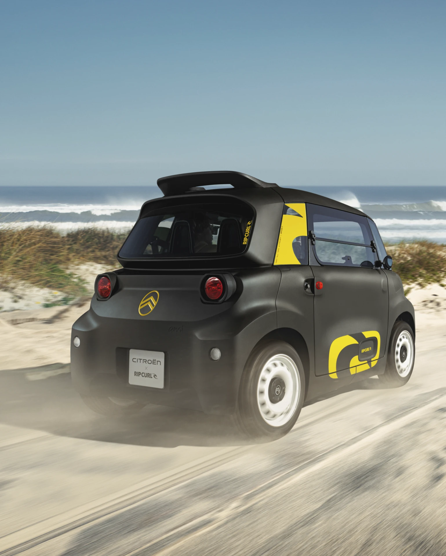 Driekwart achteraanzicht van de Citroën Ami x Rip Curl rijdend, elektrische auto zonder autorijbewijs, met speels rijden in de stad.