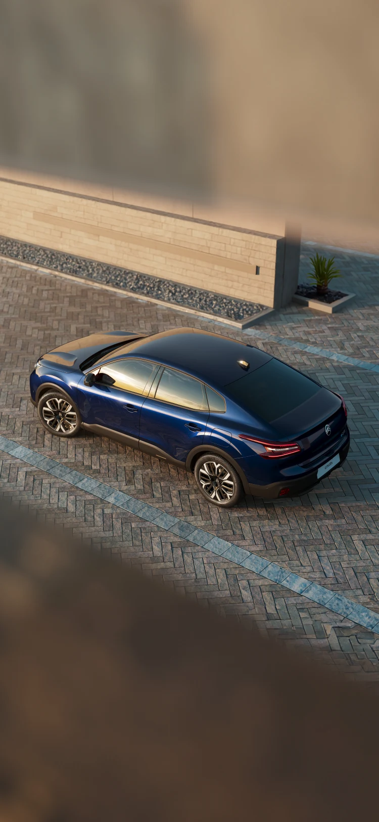 Bovenaanzicht schuin achter van de Citroën ë‑C4 X geparkeerd op een verhard terrein in zonsonderganglicht.