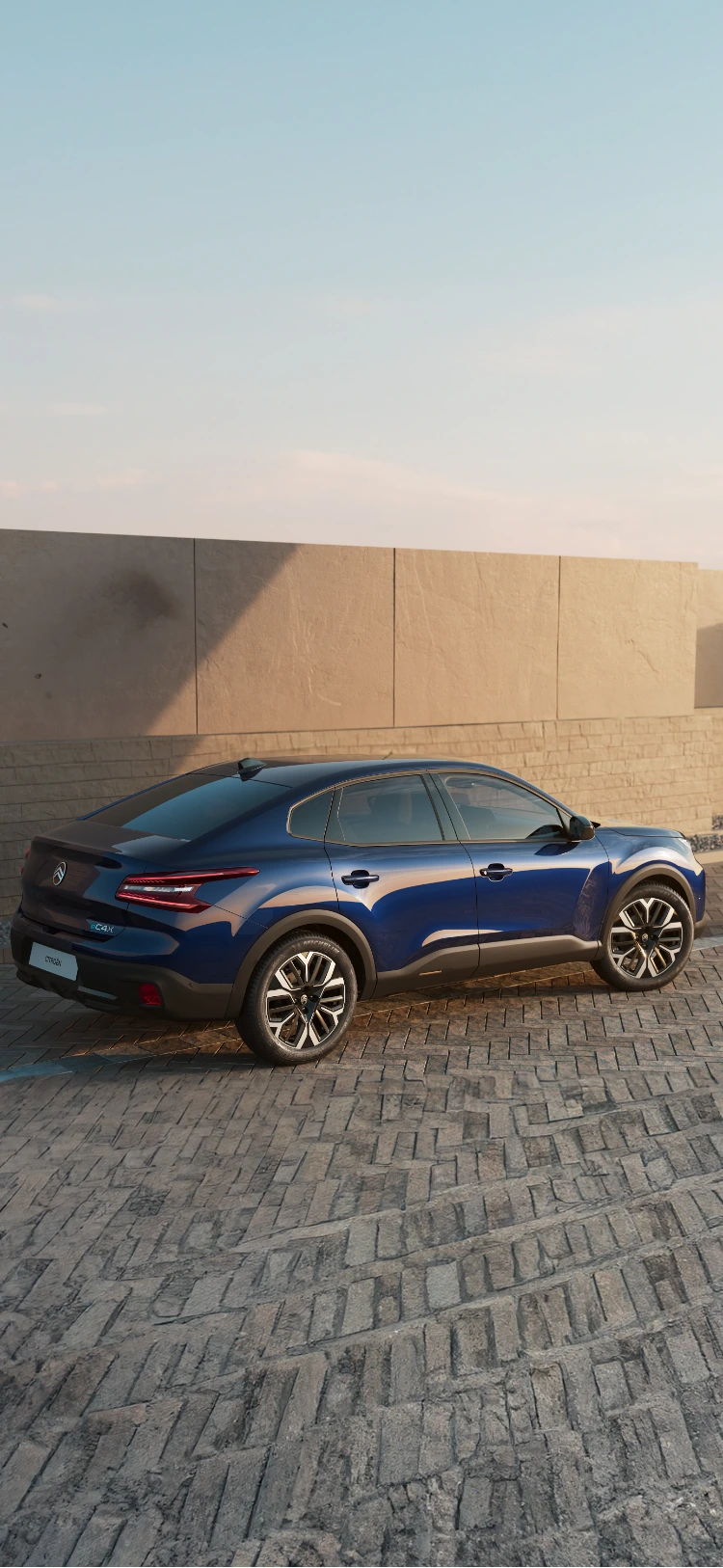 Zijaanzicht van de Citroën C4 X rijdend langs de kust bij zonsondergang met een slank profiel.
