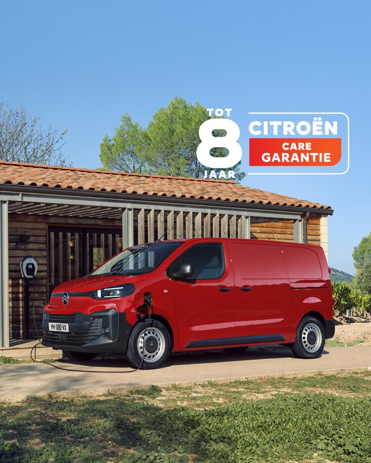 Side three‑quarter exterior view of a red Citroën ë‑Jumpy charging in front of a building, showing modern electric design, everyday practicality, connectivity and confident professional presence.